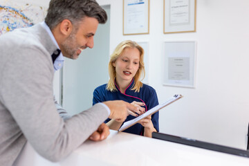 Male visitor filling out medicine documents in doctor office. Patient asking about his medical bill.