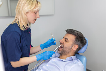 Fototapeta premium Female dentist curing teeth cavity in blue gloves. Dentist caries treatment at dental clinic office. People, medicine, stomatology and health care concept