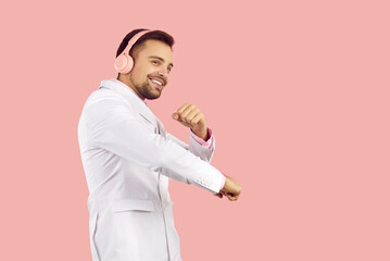 Overjoyed young man in suit isolated on pink studio background wear wireless headphones listen to music. Smiling guy in earphones enjoy good quality sound in modern device. Technology.