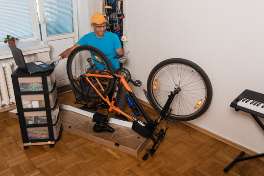 Portrait of man repairing bicycle home and looking at his modern laptop