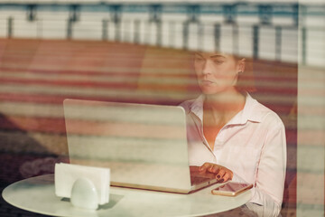 Young beautiful girl sitting in cafe and working on computer. concept of remote work, which has...