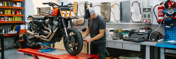 Photo sur Plexiglas Moto Unrecognizable mechanic man checking engine of custom motorcycle over platform on factory