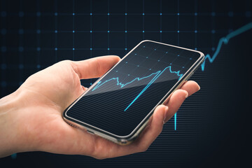 Close up of female hand holding mobile phone with growing blue financial forex chart on dark grid background. Stock, economy, market and trade concept.