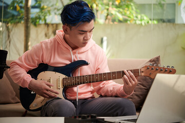 Portrait of young man concentrated on playing electric guitar and practising new chord