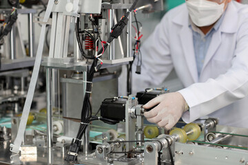 Worker hands in personal protective equipment or PPE inspecting quality of mask and medical face mask production line in factory, manufacturing industry and factory concept.