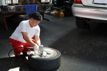 Man technician car mechanic in half uniform holding tire for replacement or changeing at repair garage. Happy asian worker smiling and looking at camera. Concept of car center repair service.