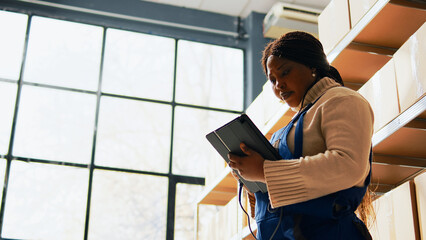 Woman working with scanner and tablet in storage room, scanning cardboard packages with barcodes in depot. Female worker checking boxes with merchandise and products, quality control. Handheld shot.
