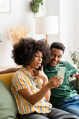 Black couple using smartphone on sofa