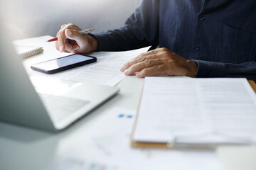 Asian businessman using a smartphone and working with  laptop while sitting at desk, Lawyer review contract, document of insurance in office