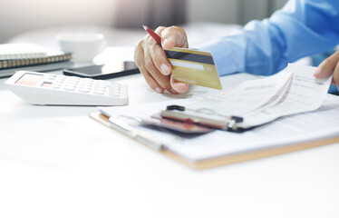 Asian businessman holding credit card to checking invoice and use calculator to calculate cost from online order, A man start new business online and using a credit card to pay for order