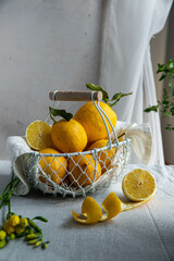 Fresh lemons in white wire basket on bright background in warm light.