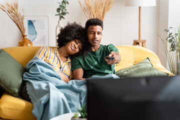 Cheerful black couple watching movie on sofa at home