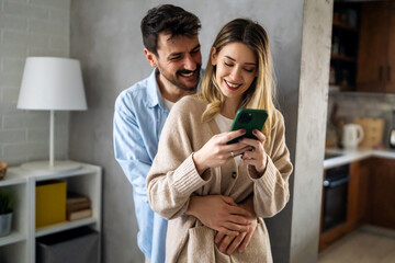 Smiling couple embracing while looking at smartphone. People sharing social media on cellphone.