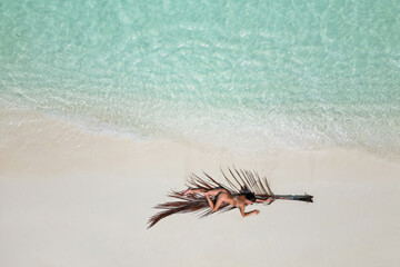 young woman tanning sunbathing on palm tree leaf woman wearing bikini at the beach on a white sand from above view from drone