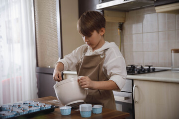 Little boy preteen makes homemade cupcakes at domestic kitchen. Family activities with children. Child baking muffins.