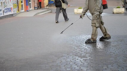 Man in protective suit spraying antiseptic solution on sidewalk in city. Persona disinfecting spray chemicals to preventing spread coronavirus. Sanitary measures in public place. Coronavirus pandemic