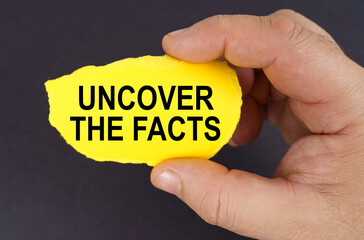 On a black background, in the hands of a man, a yellow torn cardboard with the inscription - Uncover the Facts