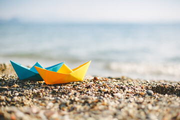 Fototapeta na wymiar Blue and yellow paper boats on the pebble beach