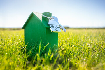 House key on a house shaped keychain with green wooden eco home on grass