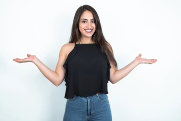 Cheerful cheery optimistic young brunette woman wearing black blouse over white studio background holding two palms copy space