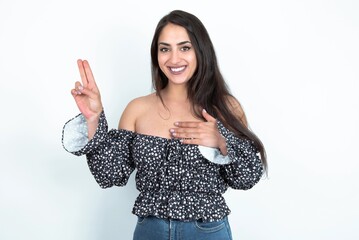 young brunette woman wearing a blouse over white studio background smiling swearing with hand on chest and fingers up, making a loyalty promise oath.