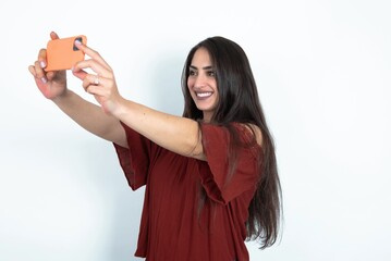 young brunette woman wearing red blouse over white studio background taking a selfie to post it on...