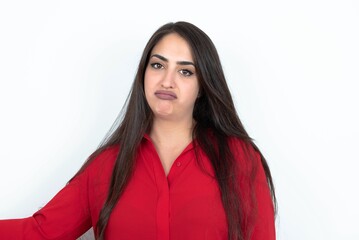 Displeased Young brunette woman wearing red shirt over white studio background frowns face feels unhappy has some problems. Negative emotions and feelings concept