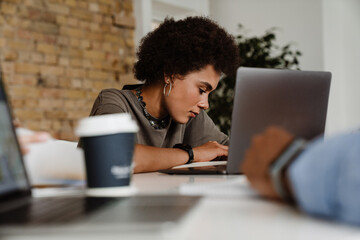 African woman working on laptop computer while sitting in office