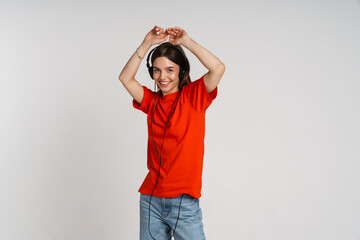 Cheerful woman listening music with headphones and dancing isolated over white background