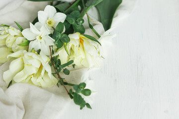 Happy Mothers day. Beautiful white tulips and daffodils on soft fabric on rustic wooden table with space for text. Stylish spring bouquet from garden. Womens day