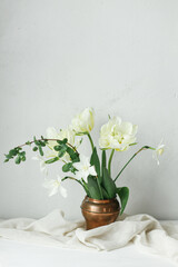 Happy Mothers day. Beautiful white tulips and daffodils in vintage vase on wooden table against rustic wall. Stylish simple spring bouquet, floral still life. Womens day. Space for text