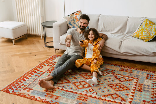 Father And Son Watching TV Together While Sitting In Living Room