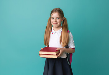 Smiling little blonde girl 10-12 years old in school uniform with backpack holding books isolated on pastel blue background studio portrait. The concept of children's lifestyle. Education at school.