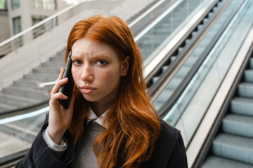 Upset woman talking on mobile phone while standing on escalator
