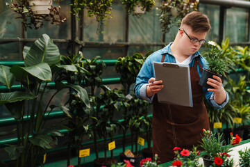 Man with down syndrome writing down notes in clipboard while working with plants in greenhouse
