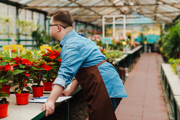 Fototapeta na wymiar Man with down syndrome standing near plants while working in greenhouse