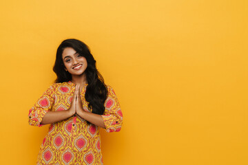 Beautiful indian woman doing namaste gesture while standing isolated over yellow background