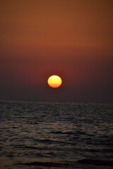 Vibrant sunset descending on the horizon, sea in golden colors, small waves gently touching the sands,