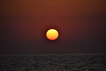 Vibrant sunset descending on the horizon, sea in golden colors, small waves gently touching the sands,