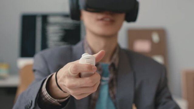 Closeup of young Asian software engineer pressing button on controller while experiencing with virtual reality in office