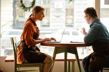 Woman using laptop while training young man with down syndrome to work in cafe