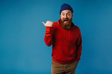 Naklejka premium Excited man pointing finger away at copy space isolated over blue background