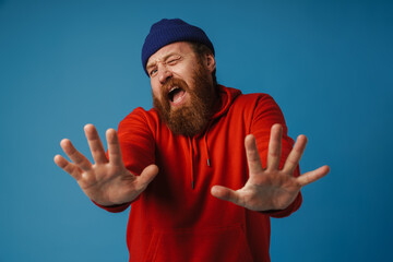 Fototapeta premium Disgusted man showing stop sign with palms isolated over blue background