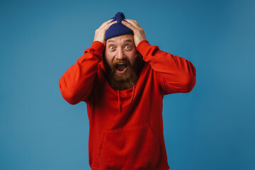 Emotional man screaming and grabbing his head in panic isolated over blue background