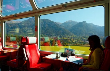 Tourists riding on Glacier Express, enjoying the idyllic scenery of Swiss countryside thru the wide...
