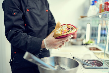 The cook preparing wrapped pita sandwich for take away. Chef cooking traditional Greek gyros for lunch