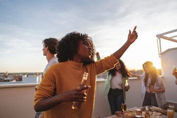 Multi ethnic group of friends hanging out at a rooftop dinner party - Multiracial young people...