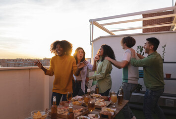 group of young people having fun at home on the roof terrace dancing and drinking alcohol