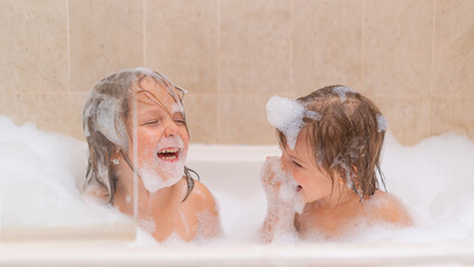 Funny sisters - baby girls playing with Soap Foam in the bath. Fun and children hygiene concept