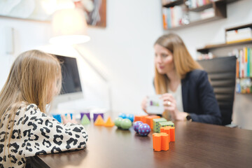 Assessment of children's mental development. Unidentified female professional psychologist observing young child playing with logic game, assessing her readiness for school, free space.